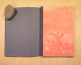 An open book. The inside page shows a pink-red image of a tree in graveyard. 