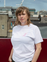 An artist wears a white t-shirt with a small pink illustration over the heart. 