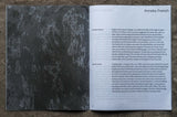 An open book on a brown background. Page on left shows a black and grey image and page on right shows a page of writing.