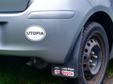 A white oval car bumper sticker with the word 'utopia' written in all caps plain black font is stuck to a silver car