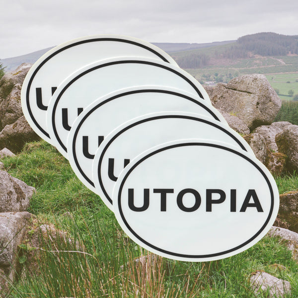 A white oval car bumper sticker with the word 'utopia' written in all caps plain black font